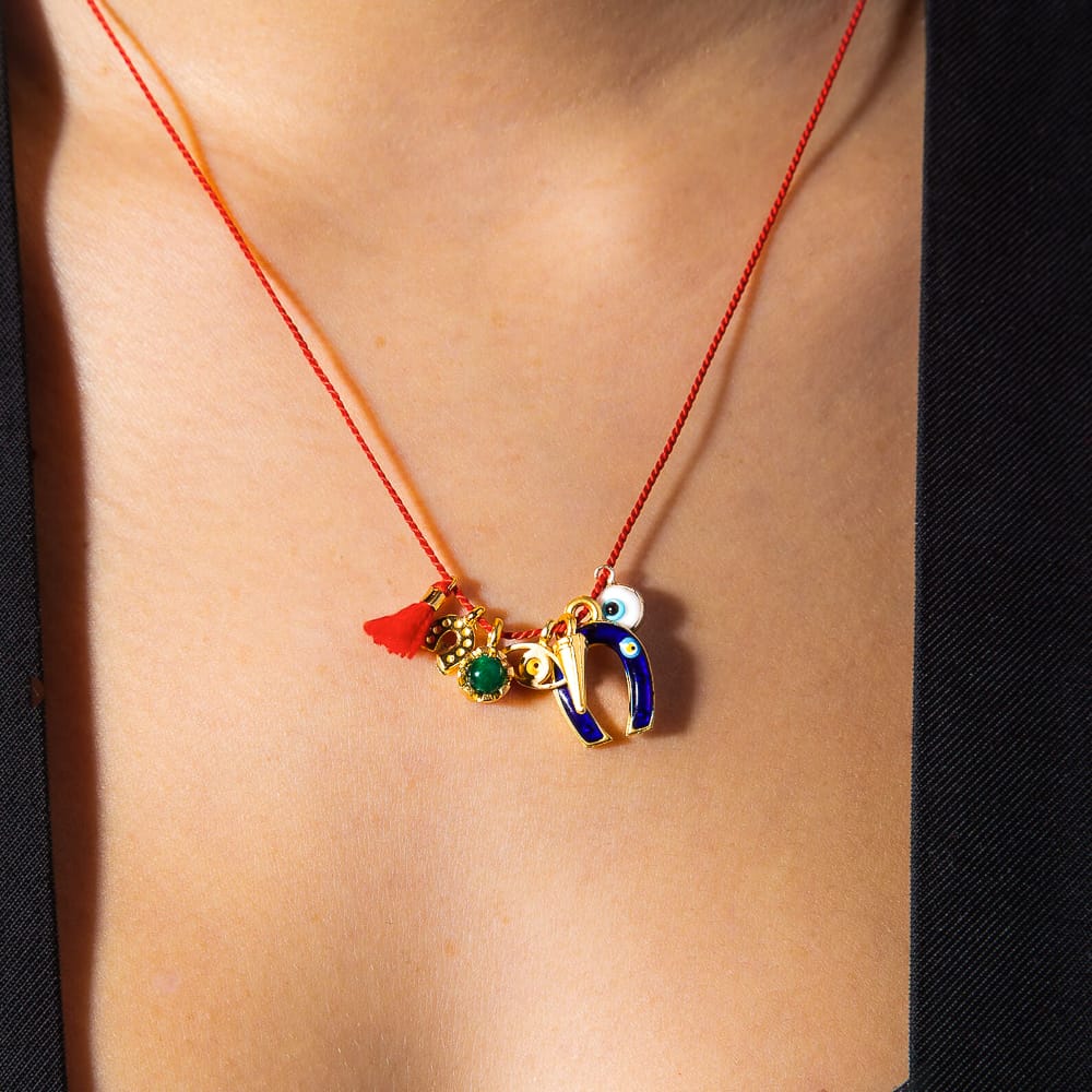 Handmade silk red string necklace with seven gold lucky charms including evil eye, horseshoe, and jade droplet, from Sunday Forever.