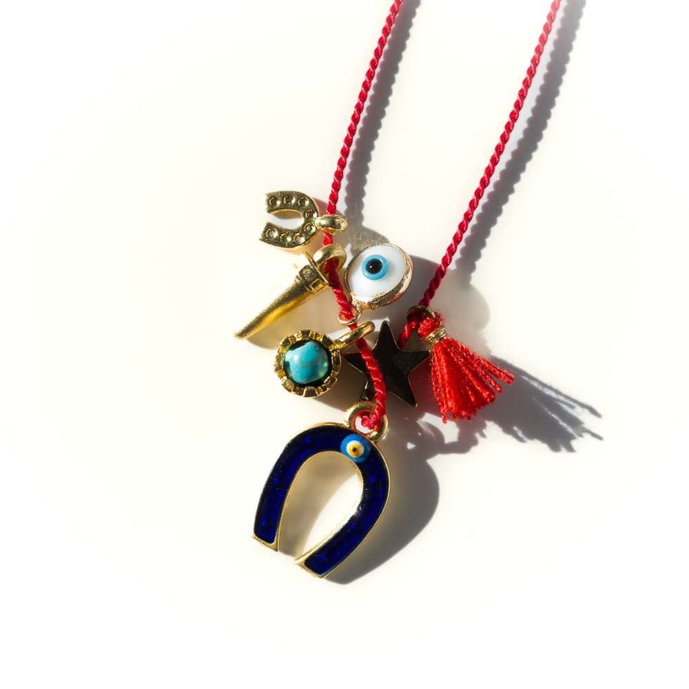 Necklace with various charms including a blue horseshoe, gold horse, and red tassel on a white background
